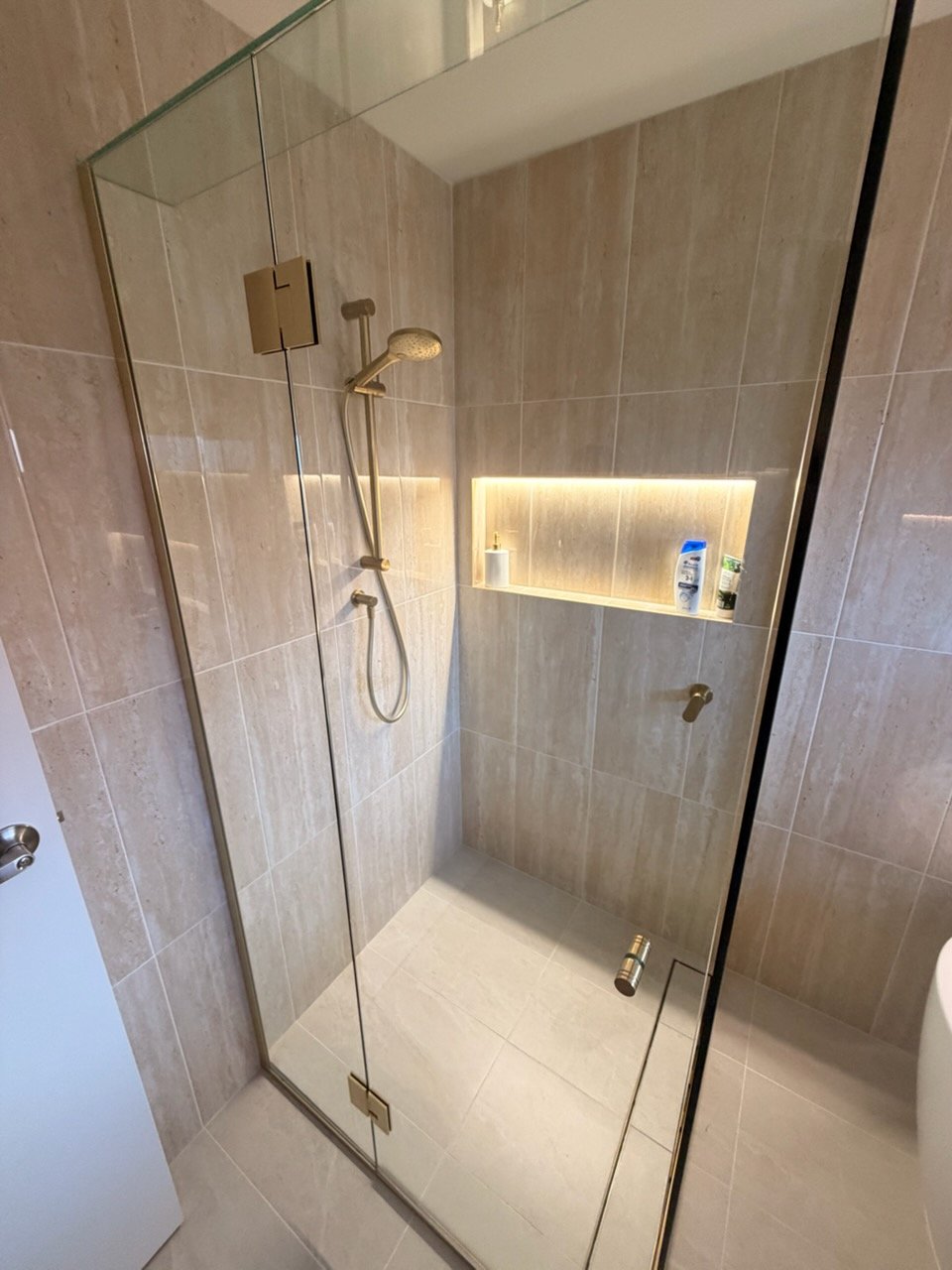 Frameless glass shower with brushed gold rail shower and illuminated tile niche installed by Scarborough Plumbing