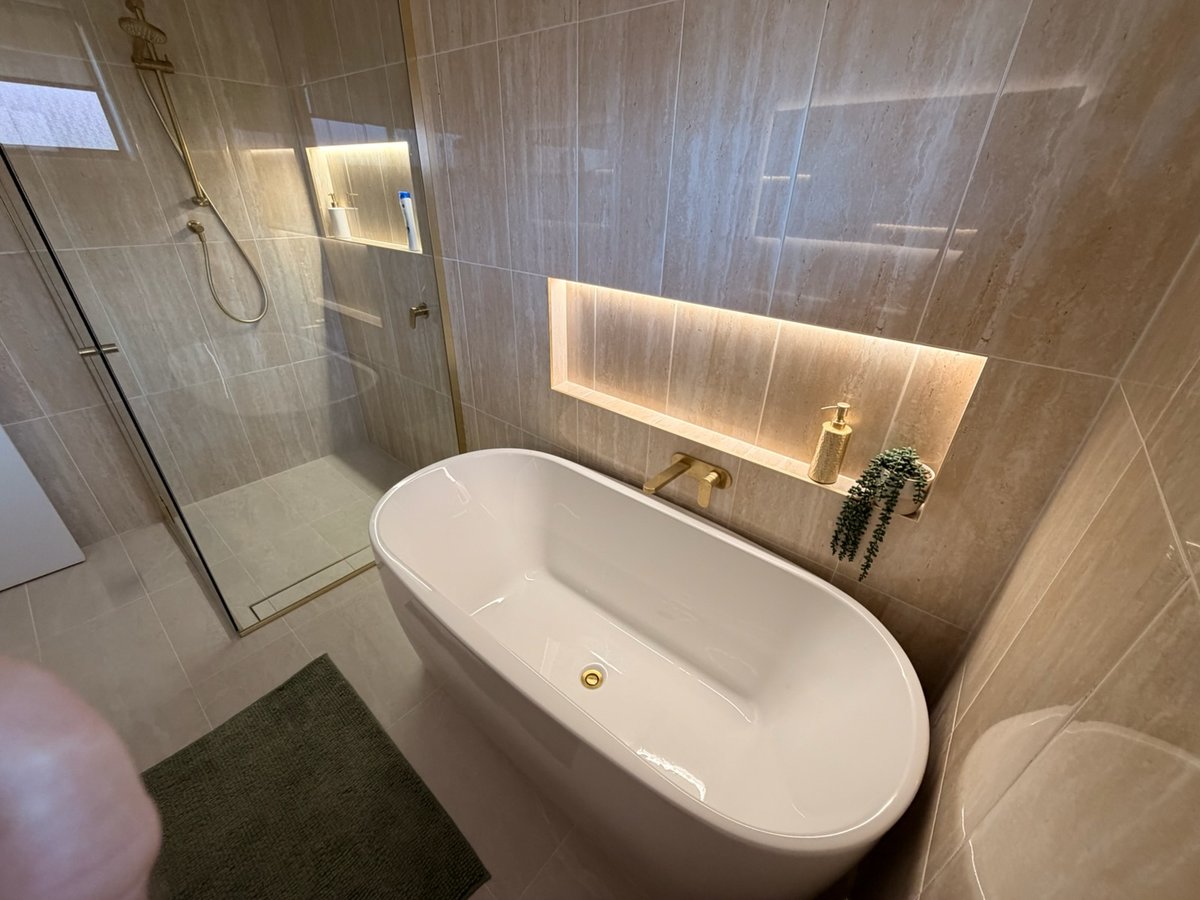 Freestanding bath with brushed gold wall-mounted tapware and illuminated tile niche in completed bathroom renovation by Scarborough Plumbing